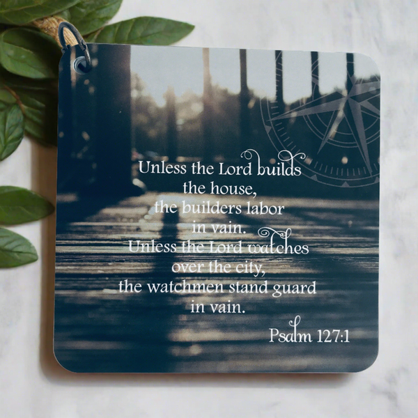 Scripture card of Psalm 127:1 printed over a photo of a deck with sunshine in the background. The scripture card is laying on a neutral background with green leaves feathered around one corner.