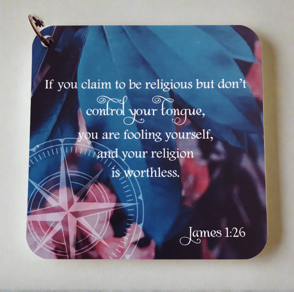 Bible verse card with James 1:26 printed over a background of leaves & pink flowers. The scripture card is laying on a neutral colored background.Encouraging bible verse for bible study.