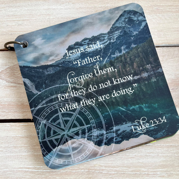 A scripture devotional card of Luke 23:34 printed over a photograph of mountains. There is a compass rose etched in the photo.