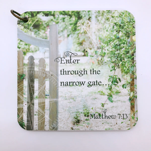 A scripture devotional card of Matthew 7:13 printed over a photo of a narrow gate and bushes. There is also a compass rose etched in the background.