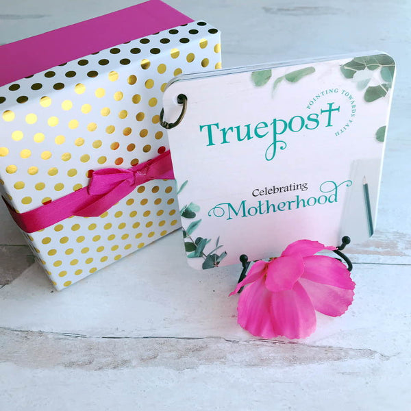 Gift box, scripture cards and iron easel displayed next to a pink flower.