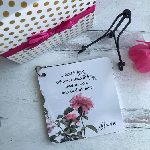 Scripture of 1 John 4:16 laying on a table next to the  easel and gift box.