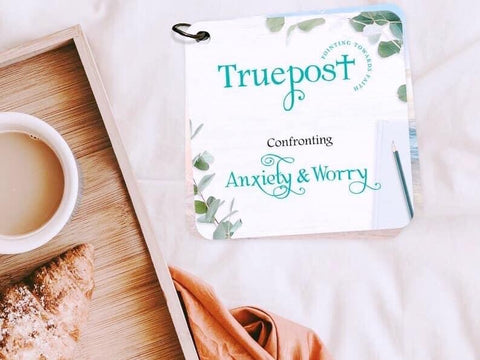 The cover of the Confronting Anxiety and worry themed scripture cards laying on a cream colored blanket next to a wooden tray with a cup of coffee.