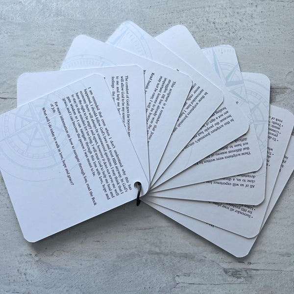 The backside of the scripture cards fanned out showing the devotions on the back of each card. Scripture devotional cards. The cards are pictured on a white rustic background.