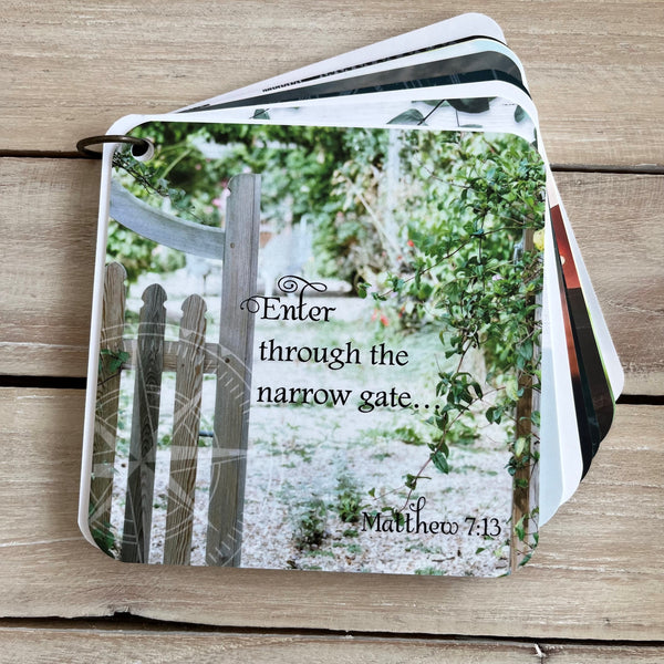 A scripture devotional card of Matthew 7:13 printed over a photo of a narrow gate and bushes. There is also a compass rose etched in the background.