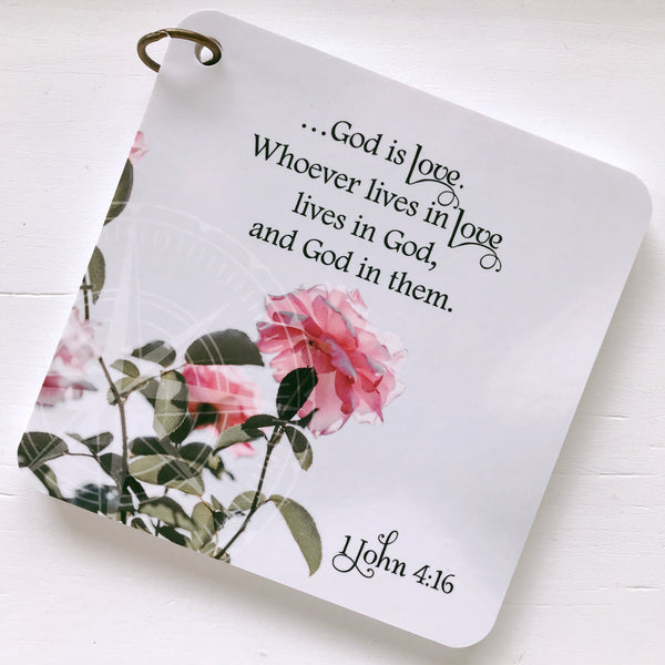 A scripture devotional card of 1 John 4:16 printed over a photo of a pink rose bush. A compass rose is etched in the background.