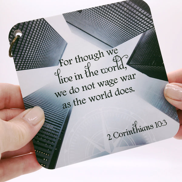 A scripture devotional card of 2 Corinthians 10:3 printed over a photo of a city skyline. A compass rose is etched in the background.
