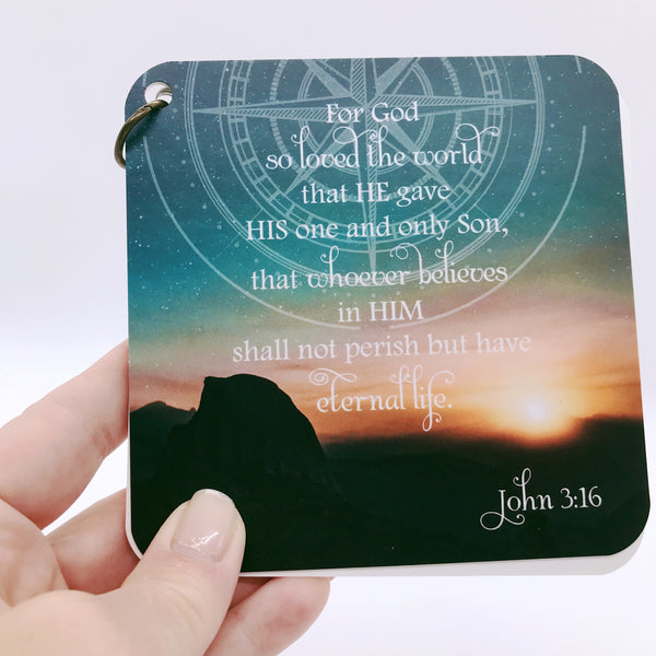 A scripture devotional card set with John 3:16 printed over the photograph of a setting sun over a dessert. There is a compass rose etched in the background of the photo.