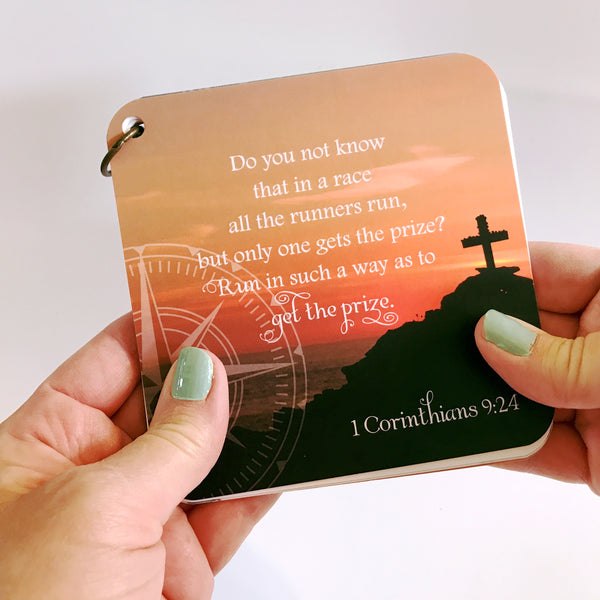 scripture devotional card of 1 Corinthians 9:24 printed over a sunset scene of a cross on a hill. Uplifting message card.