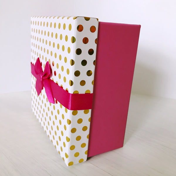 This is a side view of the gift box. Shows the hot pink bottom, the cover with a white background and gold metalic dots, with a hot pink bow.
