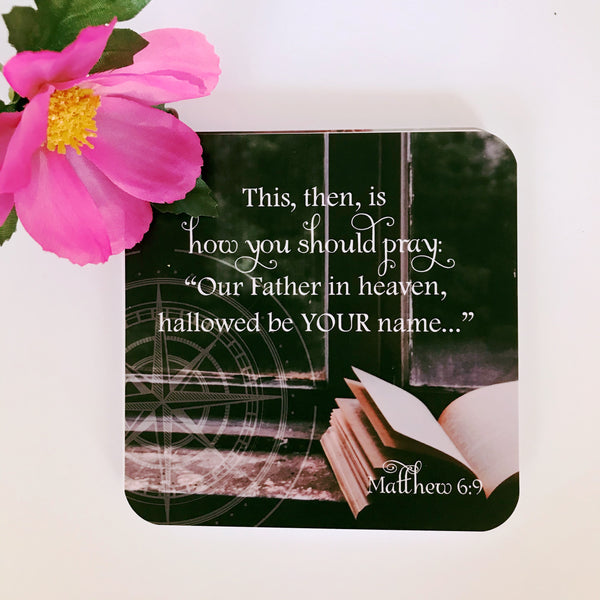 Scripture card with Matther 6:9 printed over a photo of a Bible sitting next to a window.