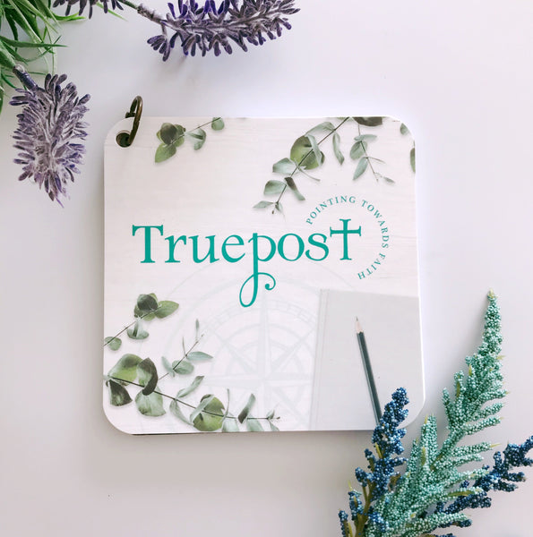 Truepost scripture devotional card set laying on a white table with spring flowers of purple and turquoise.