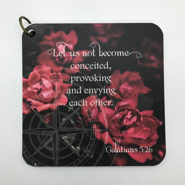A scripture devotional card with Galatians 5:26 printed over a photo of blooming red flowers , with a compass rose etched in the background.