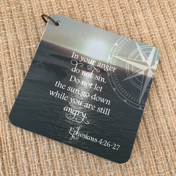 Scripture card of Ephesians 4:26-27 printed over a photo of a still body of water, with rocks pertruding from it and a setting sun as the backdrop. Daily Bible verse card.