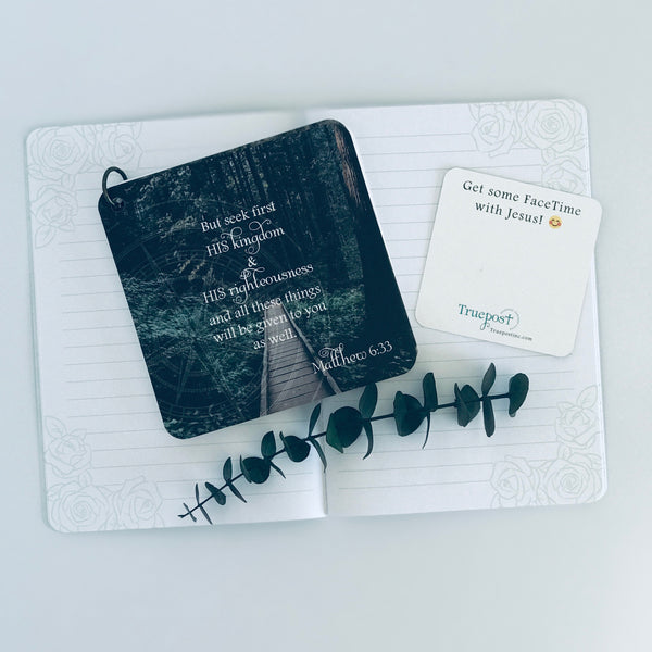 Scripture card of Matthew 6:33 is printed over a photo of a small, narrow, wooden bridge through a lush green forest. The card is laying on top of an open journal next to a card that says get some Facetime with Jesus. 