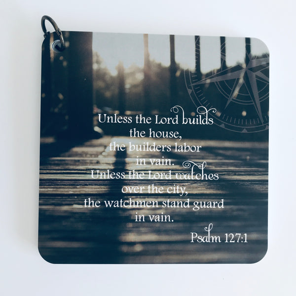 Scripture card of Psalm 127:1 is printed over a photo of what looks like the rod iron fence railing around a wooden deck, with the sun peeking through the rails. Bible verse card.
