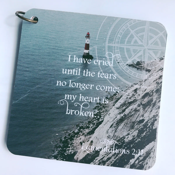 Scripture card on loss from Lamentations 2:11 is printed over a photo of a lighthouse out in the middle of a body of water with a mountain to the right side. The cards are pictured on a white background.