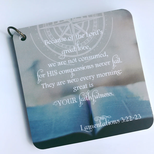 Scripture card themed around loss from Lamentations 3:22-23 is printed over what looks like an opened Bible. and the card is pictured on a white background.