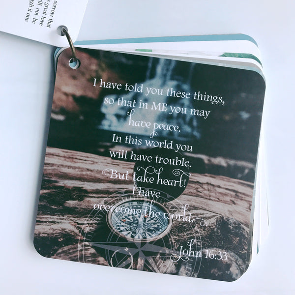 Scripture card of John 16:33 is printed over a photograph of an old compass with the cover opened. It almost looks like an old pocket watch. The card is laying on a white background