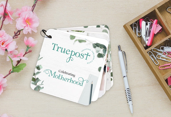 Scripture devotional cards of the Celebrating Motherhood set laying on a white background with flowers & paper clips.