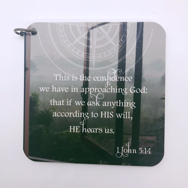 Scripture card for 1 John 5:14 printed over a photo of a window opened up over trees with a compass across the top.
