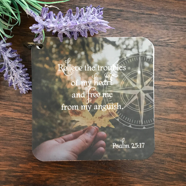 Scripture card of Psalm 25:17 relieve the troubles of my heart and free me from my anguish printed over a photo of a hand holding a leave with a heart on it.