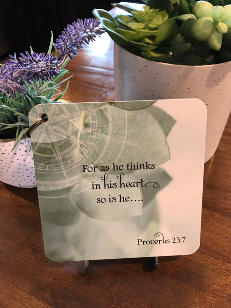 Scripture card of Proverbs 23:7 for as he thinks in his heart so is he printed over a photo of eucalyptus.